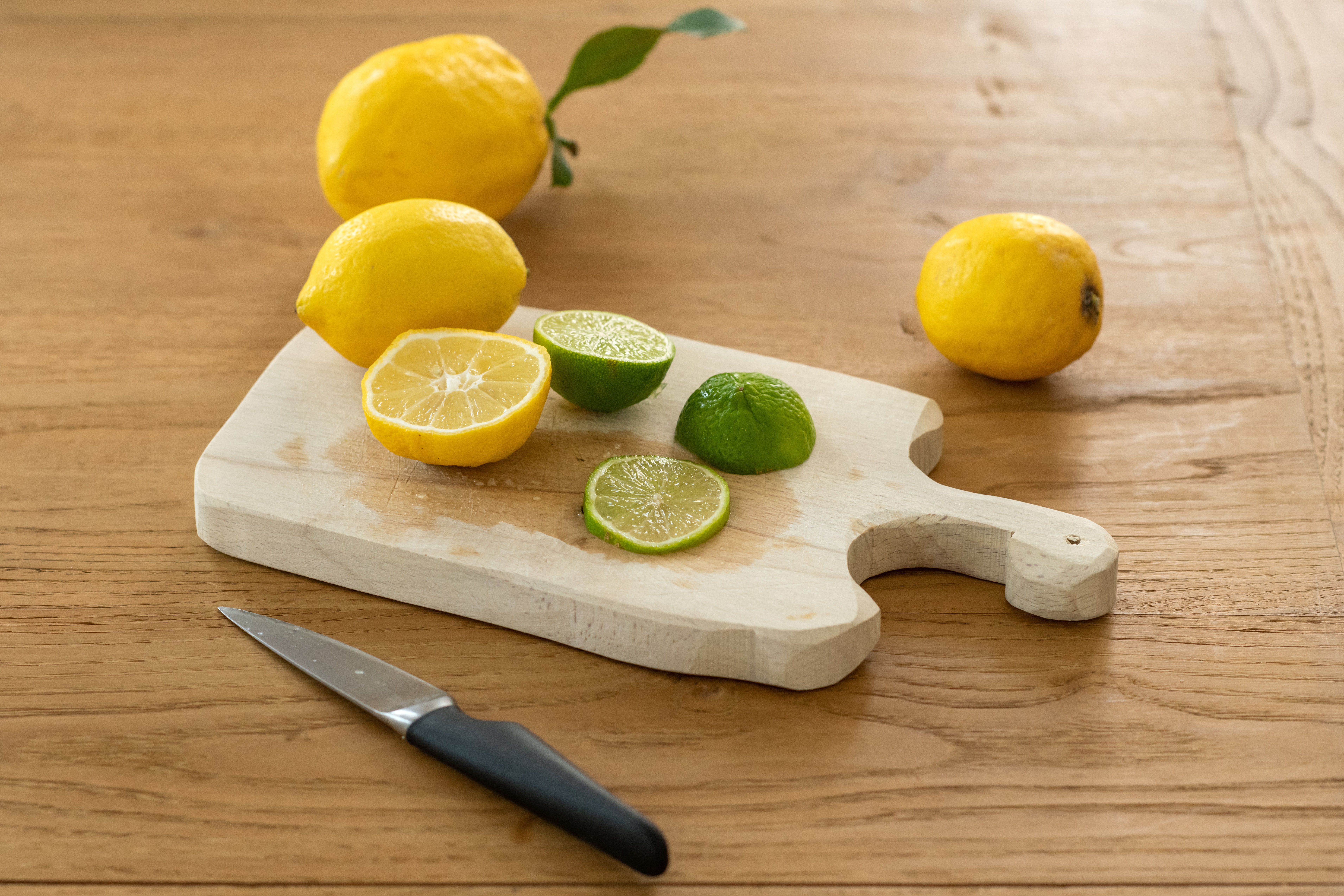 Fresh lemons on a wooden chopping board with a knife laid alongside, ready to be cleaned and prepared.